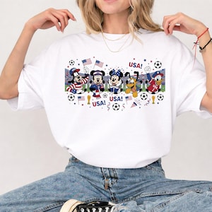 Pu&ograve; includere: T-shirt bianca con i personaggi dei cartoni animati Topolino, Minnie, Pluto e Paperino in abiti patriottici, con la scritta "USA!" e palloni da calcio. Il design incorpora bandiere americane ed elementi celebrativi.