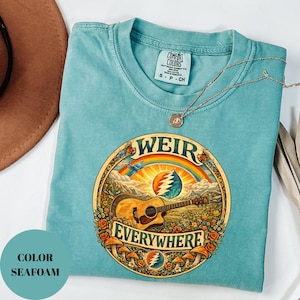 May include: Seafoam green t-shirt with a circular graphic featuring a guitar, rainbow, and the words "WEIR EVERYWHERE." The shirt has a Comfort Colors tag and a gold necklace. The colour is labelled "SEAFOAM."