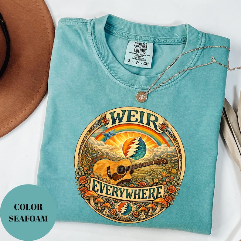 May include: Seafoam green t-shirt with a circular graphic featuring a guitar, rainbow, and the words "WEIR EVERYWHERE." The shirt has a Comfort Colors tag and a gold necklace. The colour is labelled "SEAFOAM."