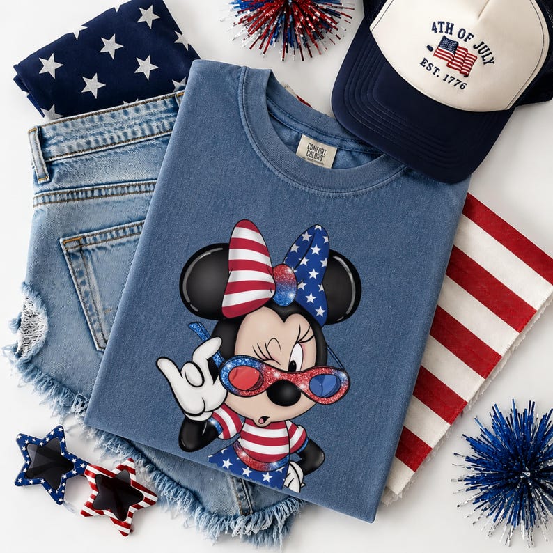 Może przedstawiać: Patriotyczny zestaw z niebieską koszulką z grafiką Myszki Minnie w kolorach czerwonym, białym i niebieskim, dżinsowymi szortami, czapką bejsbolową z napisem "4th of July", okularami przeciwsłonecznymi w kształcie gwiazd i bandaną. Na białym tle.