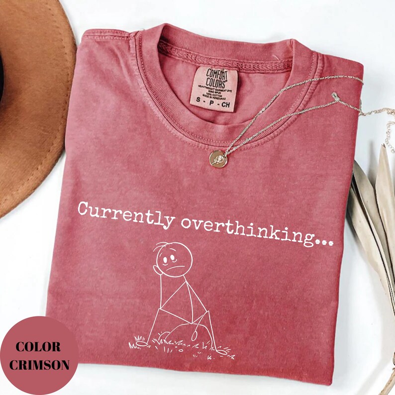 K&ouml;nnte beinhalten: Karmesinrotes T-Shirt mit dem Text "Currently overthinking..." und einer Strichm&auml;nnchen-Grafik. Das Shirt hat einen Rundhalsausschnitt und ein kleines Etikett. Eine silberne Halskette mit Anh&auml;nger liegt &uuml;ber dem Shirt.