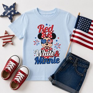 K&ouml;nnte beinhalten: Hellblaues T-Shirt mit Minnie Mouse in patriotischer Sonnenbrille und Schleife. Der Text "Red White & Minnie" ist ebenfalls abgebildet. Rote Turnschuhe, Jeansshorts und eine kleine amerikanische Flagge sind ebenfalls im Bild.