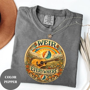 May include: A grey Comfort Colors t-shirt with a circular graphic featuring a guitar, rainbow, and the words "WEIR EVERYWHERE." The design includes flowers and mushrooms. A silver necklace is draped across the shirt.