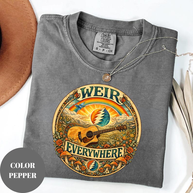 May include: A grey Comfort Colors t-shirt with a circular graphic featuring a guitar, rainbow, and the words "WEIR EVERYWHERE." The design includes flowers and mushrooms. A silver necklace is draped across the shirt.