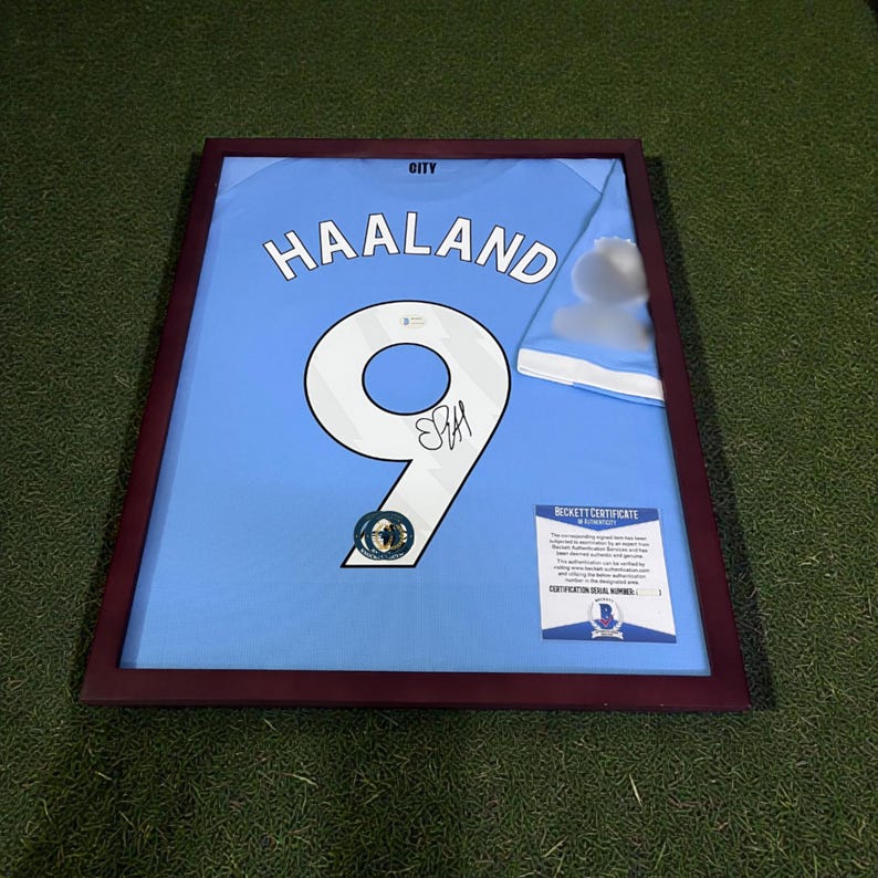 Pu&ograve; includere: Maglia da calcio azzurra incorniciata con il nome "HAALAND" e il numero "9" in bianco. La maglia &egrave; firmata e include un certificato Beckett. La cornice &egrave; di colore marrone scuro.