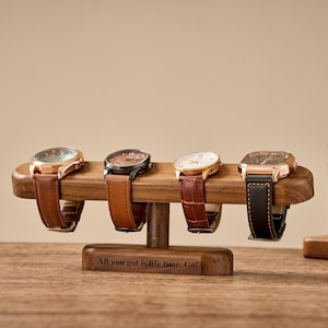 Puede incluir: Un soporte de exhibición de relojes de madera que sostiene cuatro relojes con correas de cuero. Los relojes tienen cajas doradas y negras. El soporte tiene el texto "All you got is life time. Go!"