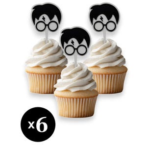 Op de afbeelding: Drie cupcakes met witte glazuur, elk bekroond met een zwart-wit gezicht op een stokje. De cupcakes zitten in een lichtbruine papieren cup. Een zwarte cirkel met het nummer "x6" staat in de linker benedenhoek.