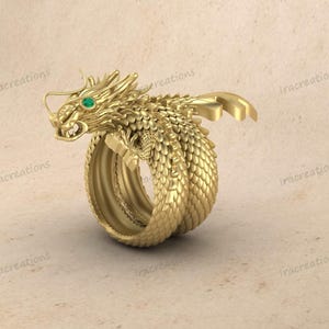 Può includere: Un anello a forma di drago dorato con dettagli intricati. Il drago presenta un occhio di gemma verde ed è avvolto attorno alla fascia dell'anello. L'anello ha un aspetto strutturato e squamoso, con un design ornato e dettagliato.