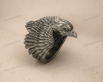 May include: A dark silver-toned metal ring featuring a sculpted eagle head and detailed wing feathers wrapping around the band. The design includes a sharp beak, defined eye, and layered plumage texture across the exterior surface of the ring.