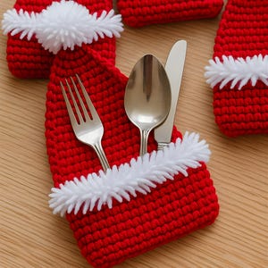 Puede incluir: Soportes para cubiertos con forma de gorro de Papá Noel de ganchillo rojo con ribete y pompones blancos. Un tenedor, una cuchara y un cuchillo se colocan dentro de uno de los soportes. Decoración festiva navideña.
