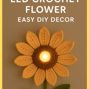 Puede incluir: Un girasol de ganchillo con una luz LED en el centro, con el texto "DIGITAL PDF PATTERN LED CROCHET FLOWER EASY DIY DECOR". La flor tiene pétalos amarillos y un centro marrón, con hojas y tallo verdes.