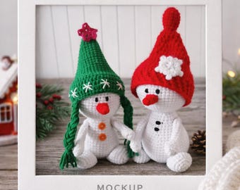 Puede incluir: Dos muñecos de nieve de ganchillo hechos a mano dentro de un marco blanco. Uno lleva un gorro verde con una estrella roja y detalles de copos de nieve blancos. El otro tiene un gorro rojo con una flor blanca. Ambos tienen narices naranjas y detalles de botones.
