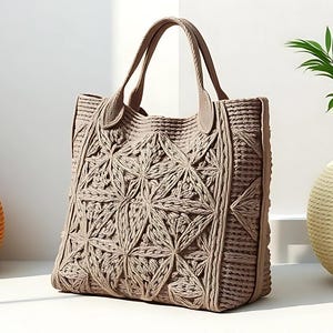 Può includere: Una borsa tote beige con un motivo geometrico, con due manici. La borsa è realizzata in materiale tessuto e si erge. Accanto alla borsa c'è un oggetto decorativo rotondo arancione e un vaso color crema con piante verdi.