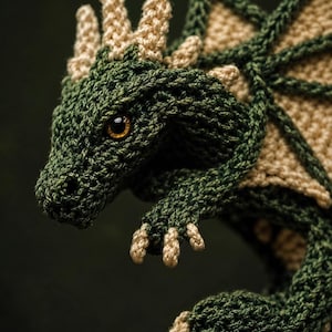 Peut inclure: Un dragon en tricot fait à la main, vert et beige. Le dragon a des écailles détaillées, un museau pointu et des yeux ambrés. Les ailes et les cornes sont beiges, contrastant avec le corps vert foncé. Un article artisanal charmant.