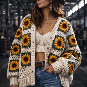 Könnte beinhalten: Cremefarbene Häkeljacke mit großen Sonnenblumen-Applikationen. Der Cardigan mit offenem Schnitt hat lange Ärmel und wird mit einem weißen Crop-Top und blauen Jeans kombiniert. Das Model trägt einen braunen Hut und Goldschmuck.