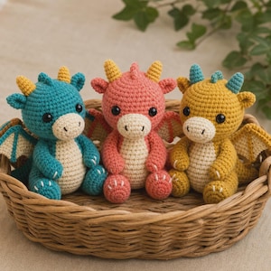 May include: Three crocheted dragon toys in a wicker basket. The dragons are in shades of blue, pink, and yellow, with cream-coloured bellies and wings. Each dragon has small horns and is sitting upright. The basket is made of light brown woven material.