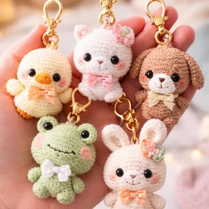 Peut inclure: Collection de six porte-clés animaux crochetés, dont un canard, un ours, un chien, une grenouille et un lapin. Chaque porte-clés est doté d'un fermoir doré et d'un nœud. Les animaux sont de couleurs pastel variées, avec des yeux noirs et des joues roses.