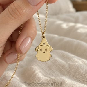 Op de afbeelding: Een goudkleurige ketting met een hanger in de vorm van een geest met een puntmuts. De geest heeft uitgesneden ogen en een kleine gegraveerde glimlach. De hanger hangt aan een fijne goudkleurige ketting. De tekst TheGentlemanTrail is zichtbaar.