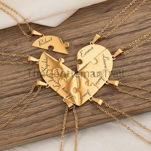 May include: Gold-colored puzzle piece necklaces arranged in a heart shape. Each piece is engraved with a name: Robert, Emma, Laura, Annie, James, Henry, Evelyn, and Sophia. The necklaces are displayed on a wooden surface.