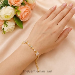 May include: A gold-toned chain bracelet featuring alternating clear, marquise-cut, and flower-shaped cubic zirconia stones. The bracelet has a delicate link design and a secure clasp, showcasing a sparkling, reflective finish on the metal surface.