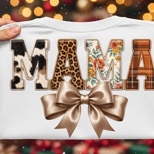 May include: A white t-shirt featuring the word MAMA in large block letters. Each letter has a unique pattern: cow print, leopard print, floral print, and brown plaid. A large, shiny, light brown satin bow is positioned below the letters.