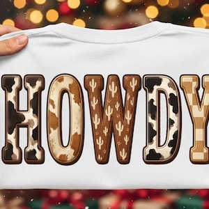 May include: A white t-shirt featuring the word HOWDY in large block letters. Each letter has a unique pattern: H has a black and white cow print, O has a brown and white cow print, W has a brown cactus print, D has a black and white cow print, and Y has a tan and white checkerboard pattern.
