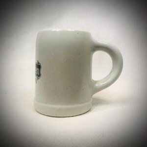 May include: A white ceramic mug with a black handle and the text "But First, Coffee" in a bold, black font. The mug is set against a blurred background, highlighting its clean design.