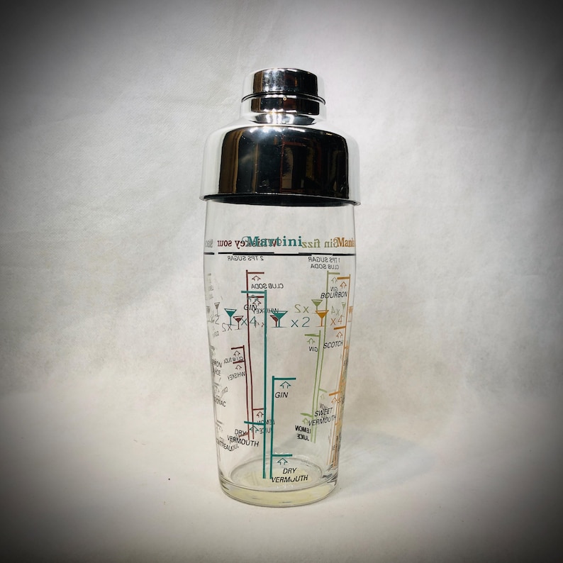 Puede incluir: Una coctelera de cristal transparente con tapa de acero inoxidable. La coctelera tiene un dise&ntilde;o impreso con recetas de c&oacute;cteles y medidas. El texto incluye "Martini" y "Bourbon".