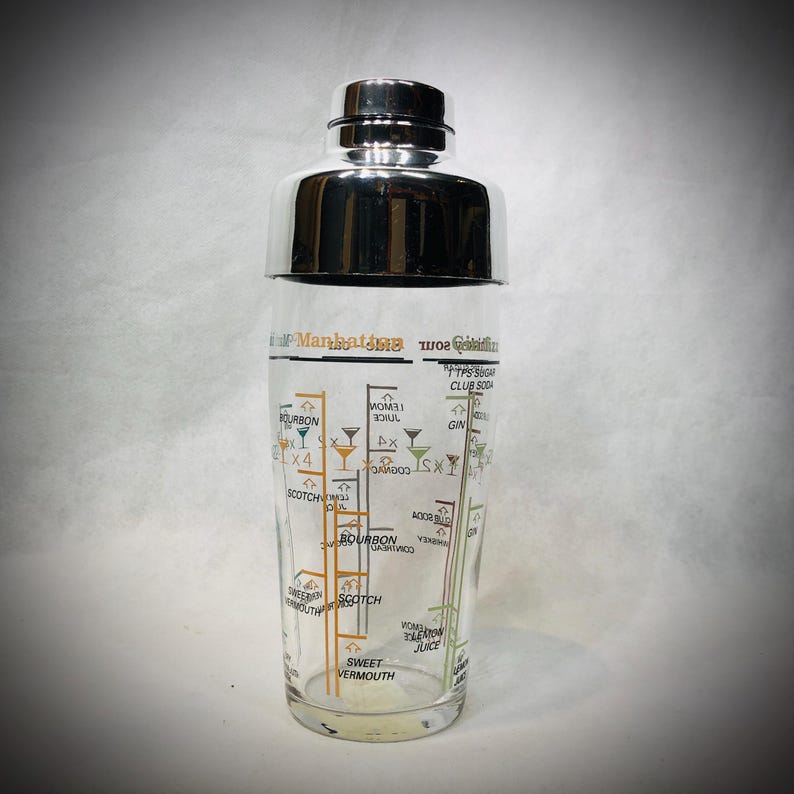 Puede incluir: Una coctelera de vidrio transparente con tapa de acero inoxidable. La coctelera tiene un diagrama de recetas de c&oacute;cteles, incluyendo bourbon, scotch y vermut. El texto "Manhattan" es visible.