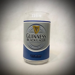 Może przedstawiać: Przezroczysty szklany kubek w kształcie puszki z etykietą Guinness Black Lager. Etykieta zawiera złotą harfę, logo Guinness i napis "St. James's Gate Dublin". Na dole etykiety znajduje się napis "Cold Brewed with Roasted Barley".