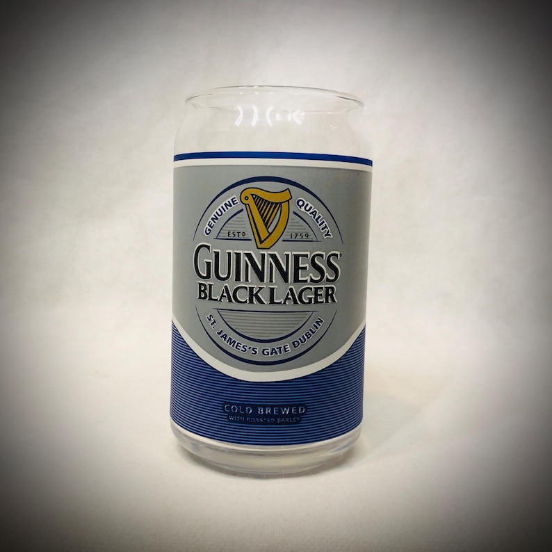 Może przedstawiać: Przezroczysty szklany kubek w kształcie puszki z etykietą Guinness Black Lager. Etykieta zawiera złotą harfę, logo Guinness i napis "St. James's Gate Dublin". Na dole etykiety znajduje się napis "Cold Brewed with Roasted Barley".