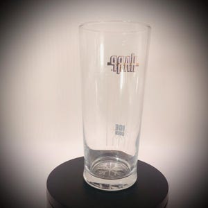 May include: A clear, tall glass with the word "Goal" in a stylized font near the top and "Cold Ice" near the bottom. The glass has a snowflake design on the bottom and is displayed on a black surface.
