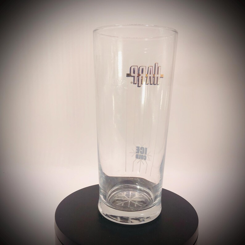 May include: A clear, tall glass with the word "Goal" in a stylized font near the top and "Cold Ice" near the bottom. The glass has a snowflake design on the bottom and is displayed on a black surface.