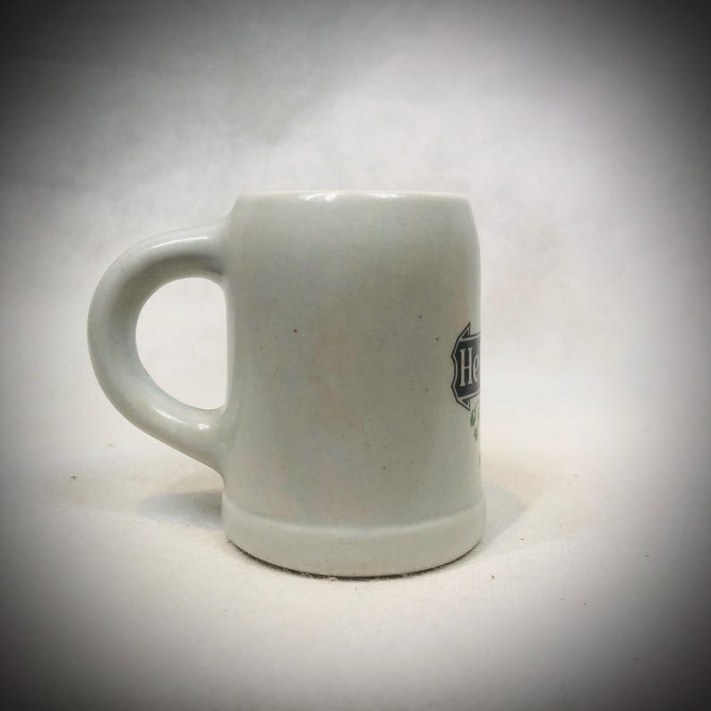 May include: A set of three ceramic mugs with a speckled, matte finish. The mugs are in shades of cream, light brown, and dark brown. Each mug has a simple, minimalist design and a rounded handle.