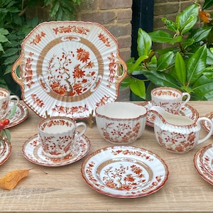 May include: An antique tea set with an orange and white floral pattern. The set includes cups, saucers, a sugar bowl, a creamer, and a large serving platter. The tea set is displayed on a wooden table.