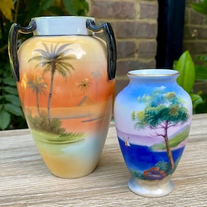 May include: Two decorative ceramic vases. One is a tall, urn-shaped vase with black handles and a painted tropical scene in orange, yellow, and green. The other is a smaller vase with a blue and green landscape design.