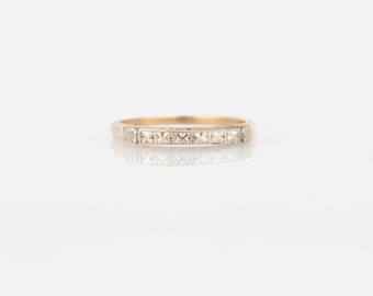 May include: A gold band ring with a row of small, clear, square-shaped stones.