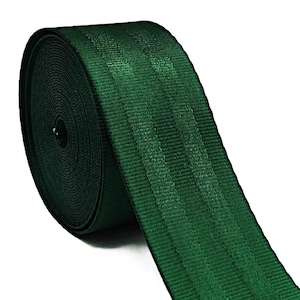 May include: A roll of dark green webbing material. The webbing has a ribbed texture and is tightly wound. The material is a solid, deep green colour, and the roll is positioned diagonally across the frame.