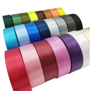 Peut inclure: Une collection de rouleaux de sangle en nylon colorés dans diverses nuances, notamment le rouge, le rose, le violet, le blanc, le bleu, le vert et le jaune. La sangle a un aspect texturé et tissé et est soigneusement enroulée. L'image présente une gamme de couleurs adaptées aux projets d'artisanat et de design.