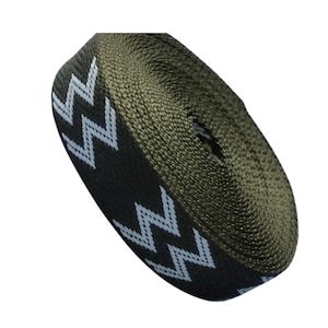 Puede incluir: Rollo de cincha verde oliva con un patrón de zigzag blanco repetido en un borde. La cincha está enrollada firmemente, mostrando la textura del material. El diseño es simple y gráfico, adecuado para manualidades.