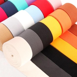 Puede incluir: Surtido de rollos de cincha tejida colorida en varios tonos, incluyendo rojo, azul, amarillo, naranja, negro y blanco. Los rollos están bien enrollados, mostrando la textura y las variaciones de color del material. Ideal para manualidades y proyectos de bricolaje.