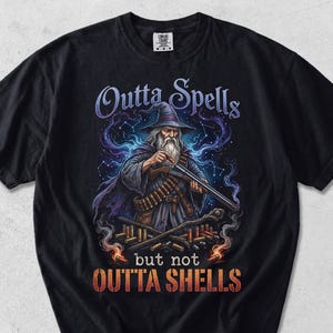 May include: Black t-shirt featuring a wizard graphic with the text "Outta Spells but not Outta Shells". The wizard is holding a shotgun. The wizard is wearing a hat and a long coat.