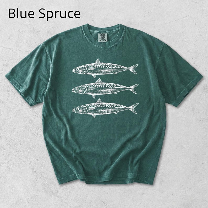 May include: A blue spruce t-shirt featuring a white illustration of three fish. The short-sleeved shirt has a crew neck and a slightly faded appearance. The text "Blue Spruce" is at the top of the image.