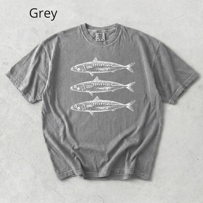 May include: Grey t-shirt with a crew neck featuring three white fish illustrations. The word "Grey" is printed in the upper left corner. The shirt is made of a soft material.