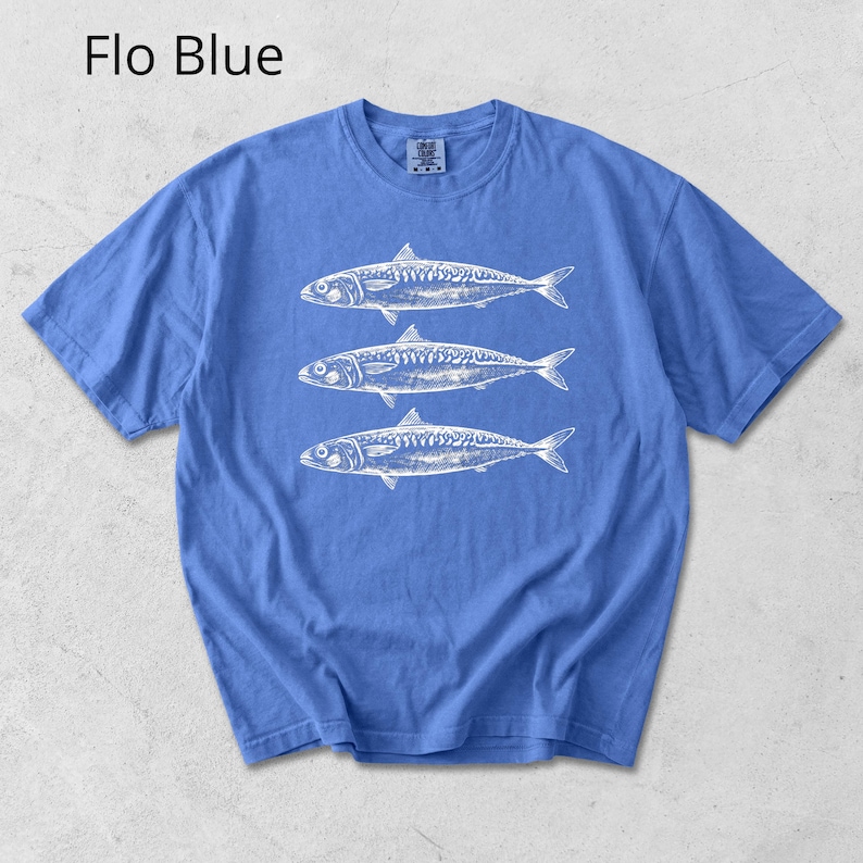 May include: A blue t-shirt with a white graphic of three fish. The text "Flo Blue" is in the upper left corner. The shirt has short sleeves and a crew neck.