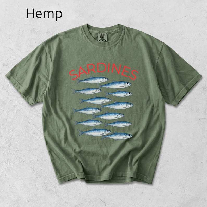 May include: Olive green t-shirt featuring the word "SARDINES" in red above a graphic of eleven blue and white fish. The word "Hemp" is printed in the upper left corner of the shirt.
