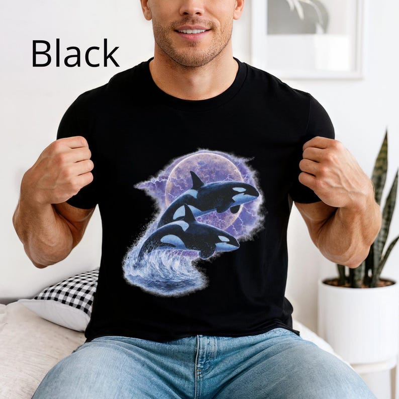 May include: Black crew neck t-shirt with a graphic of two orcas jumping from water, set against a purple moon and lightning. The word "Black" is printed in white at the top left.