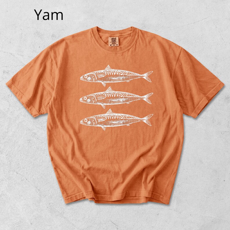 May include: Orange t-shirt with a white graphic of three fish. The word "Yam" is printed in the upper left corner. The shirt has short sleeves and a crew neck.