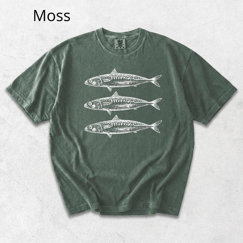 May include: Moss green t-shirt featuring a white illustration of three fish. The shirt has a classic crew neck and short sleeves. The word "Moss" is printed in the upper left corner. This casual tee is perfect for anyone who loves marine life.