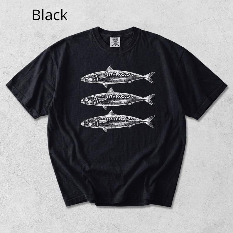 May include: Black t-shirt featuring three detailed white illustrations of fish. The fish are arranged vertically, with each one slightly overlapping the other. The shirt has short sleeves and a crew neck.